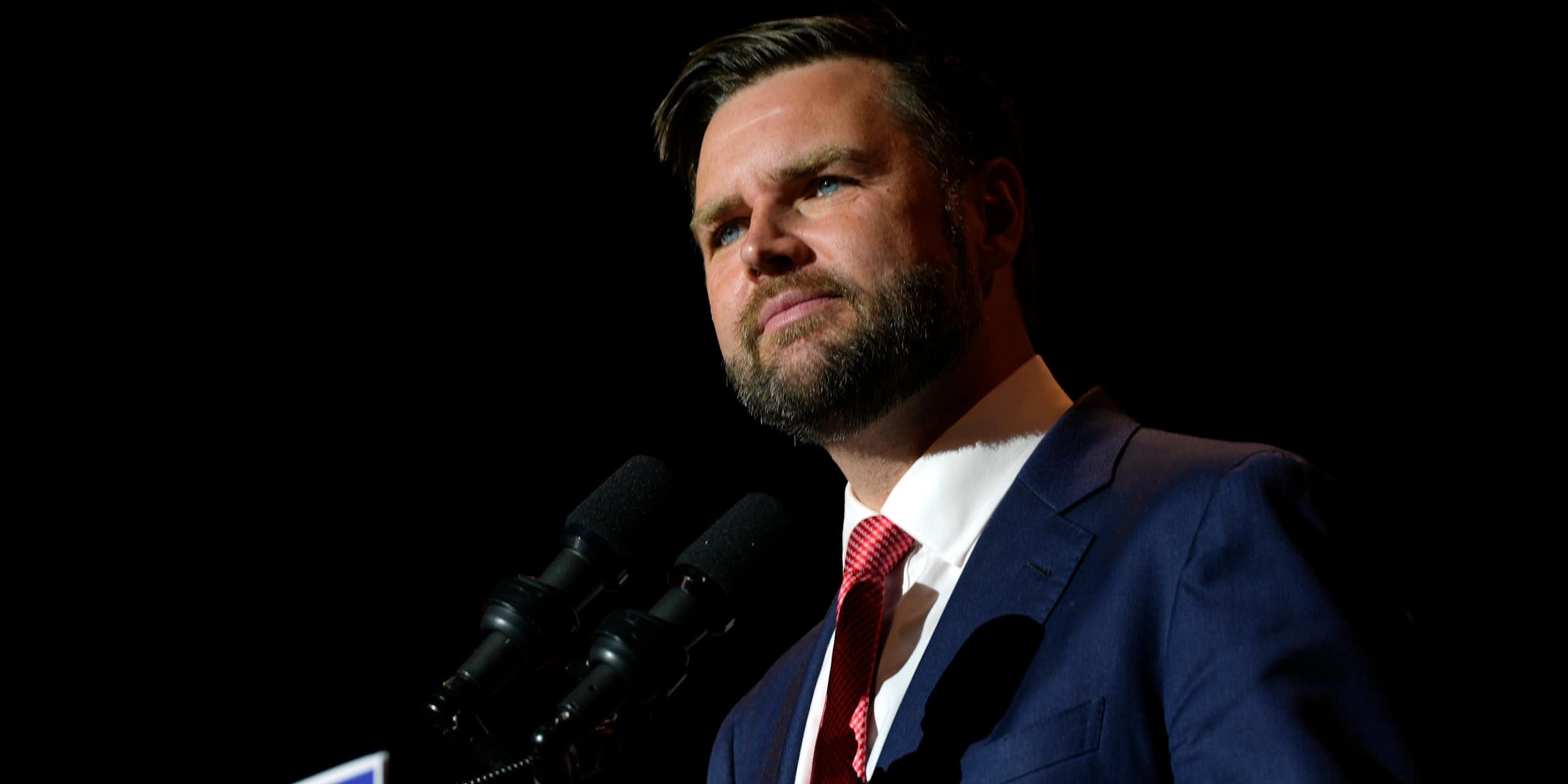 A middle-aged white man stands before a podium with a microphone on it