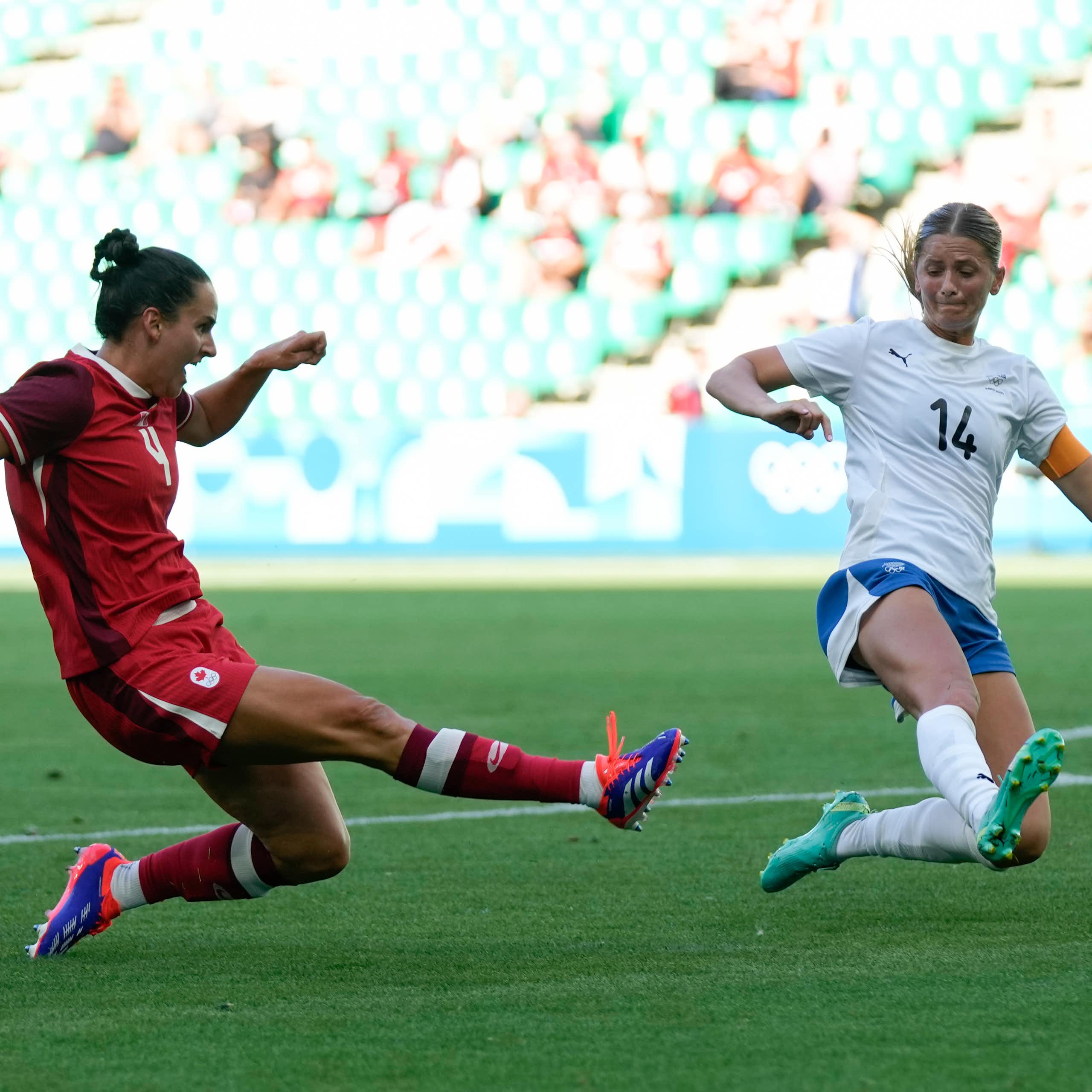 A woman in a red jersey kicks a ball while another in white attempts to deflect it