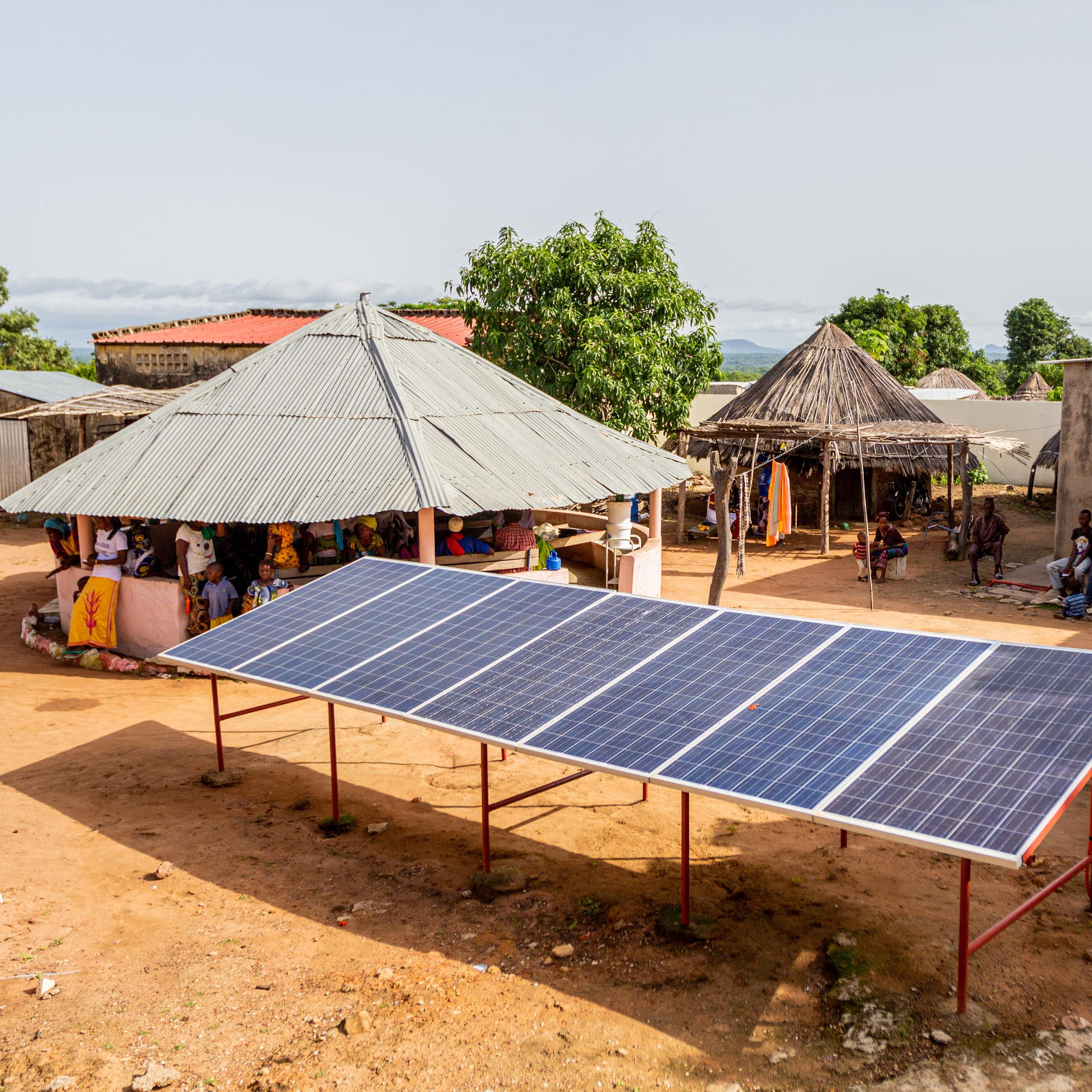 6 large solar panels mounted off the ground surrounded by huts and small houses