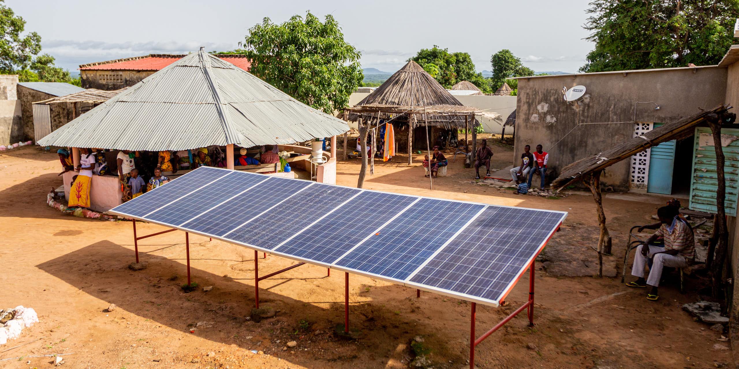 6 large solar panels mounted off the ground surrounded by huts and small houses