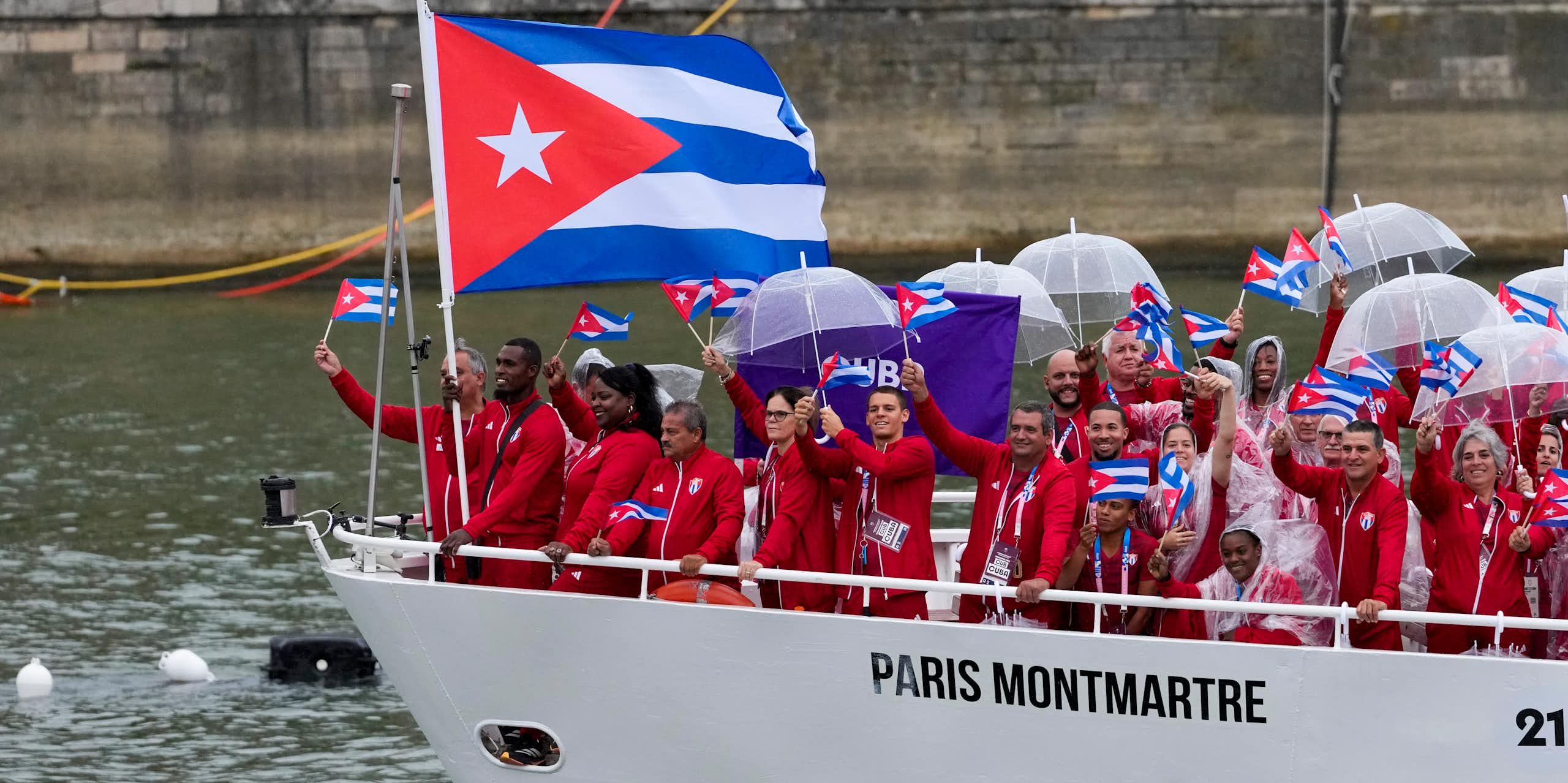 A group of people wearing red tracksuits wave Cuban flags from the prow of a white boat