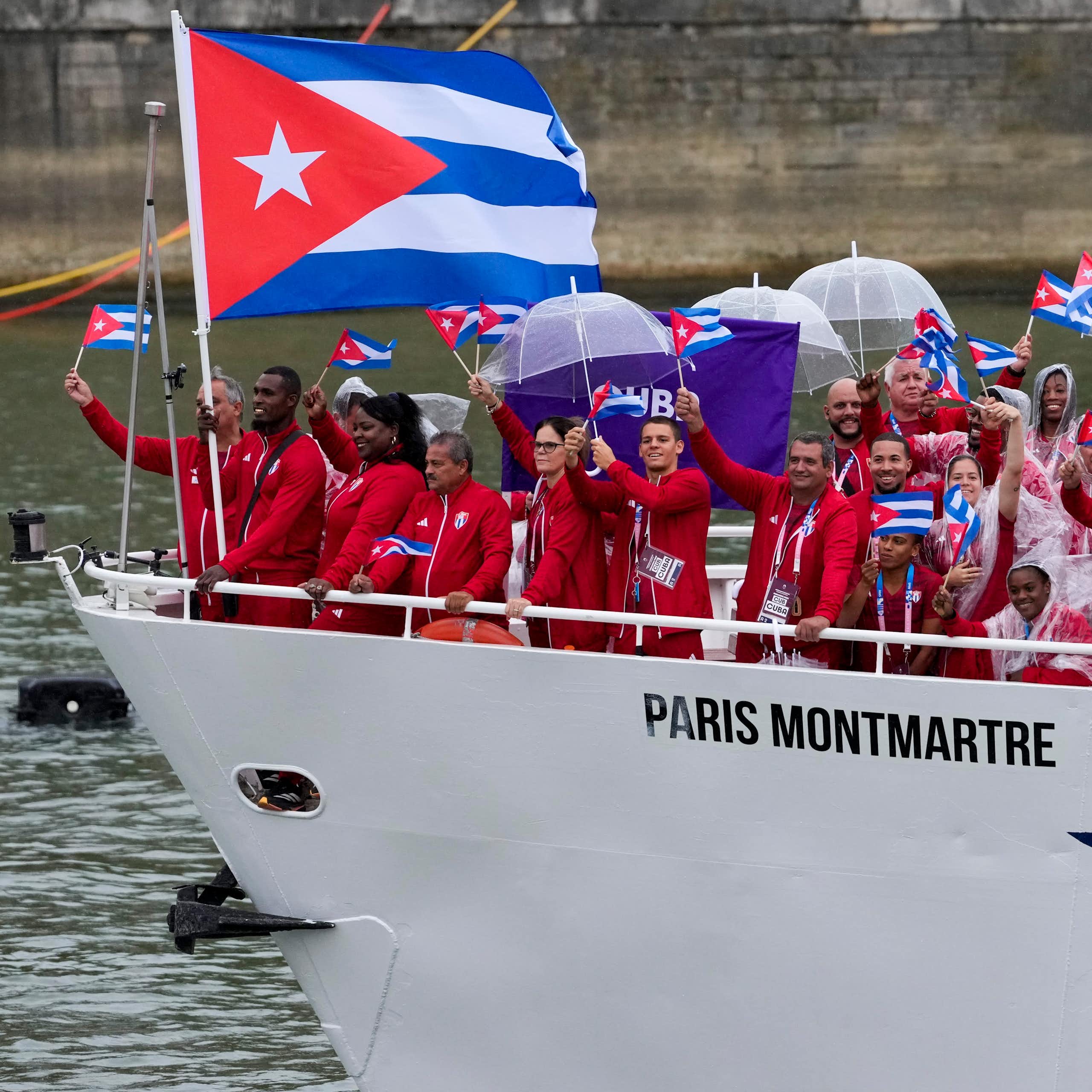 A group of people wearing red tracksuits wave Cuban flags from the prow of a white boat