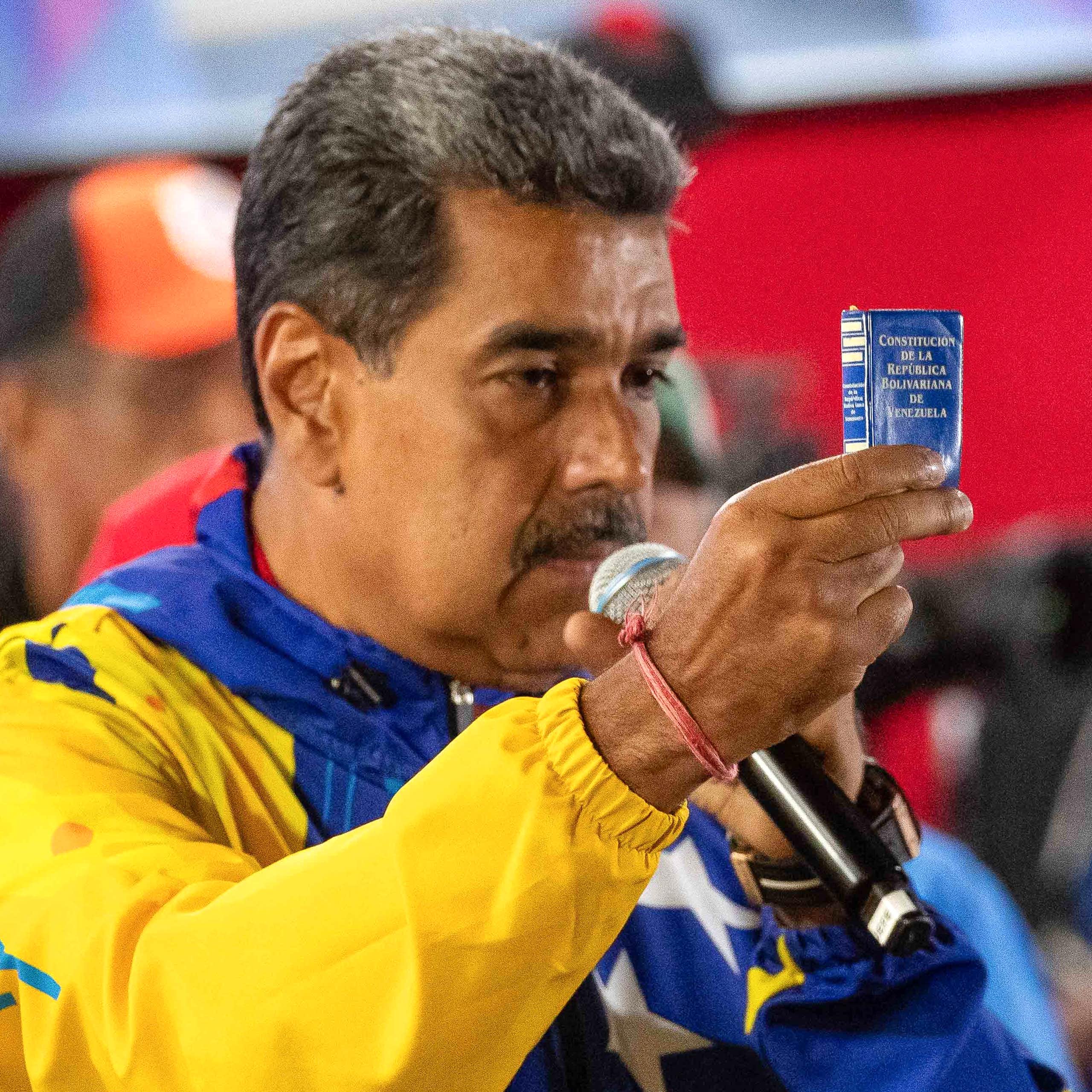 Nicolás Maduro speaking into a microphone while holding a piece of blue paper aloft.