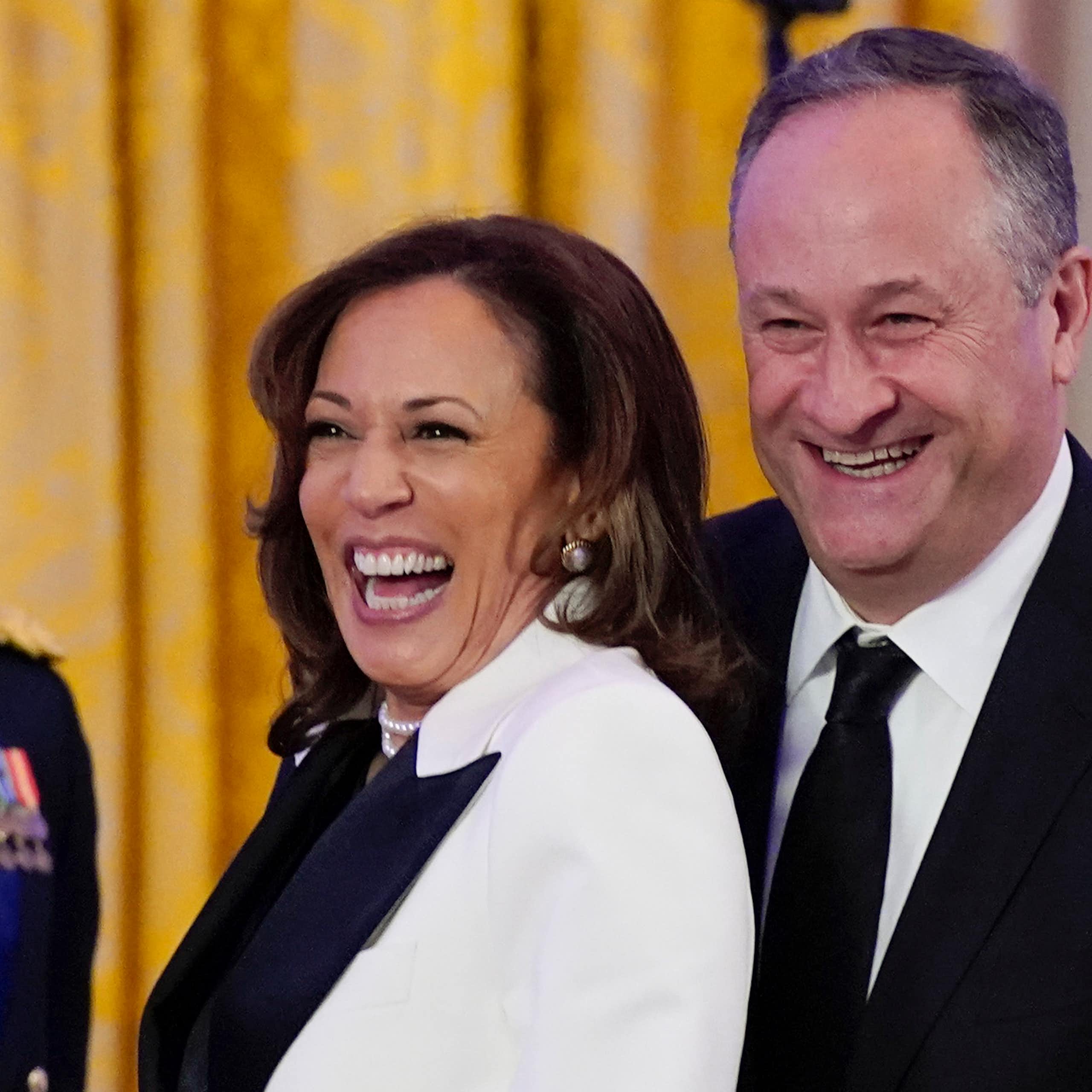 A vice-presidente dos EUA Kamala Harris sorrindo ao lado de seu marido, um homem branco de terno