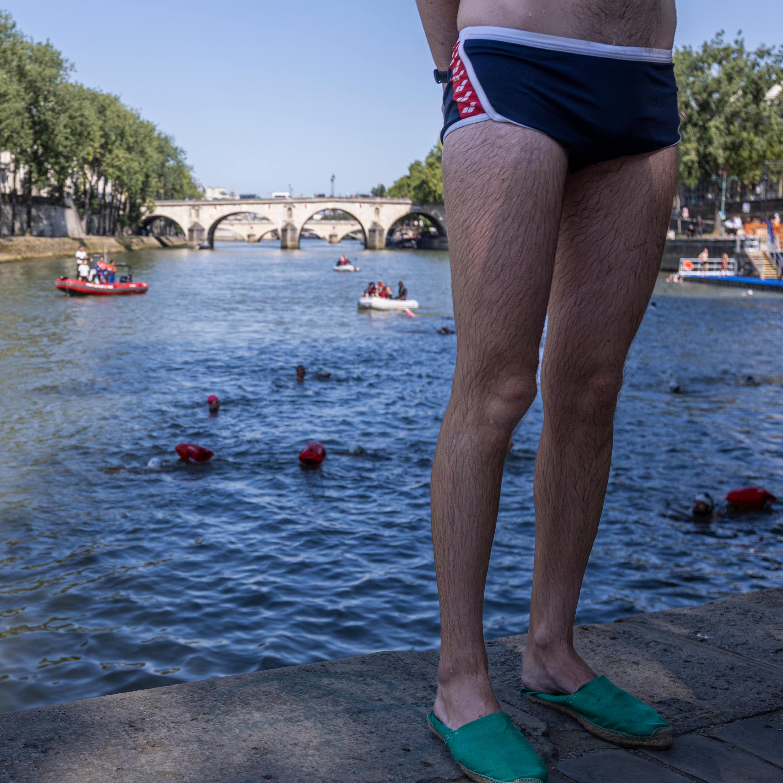 A swimmer in trunks stands on the banks of the Seine.