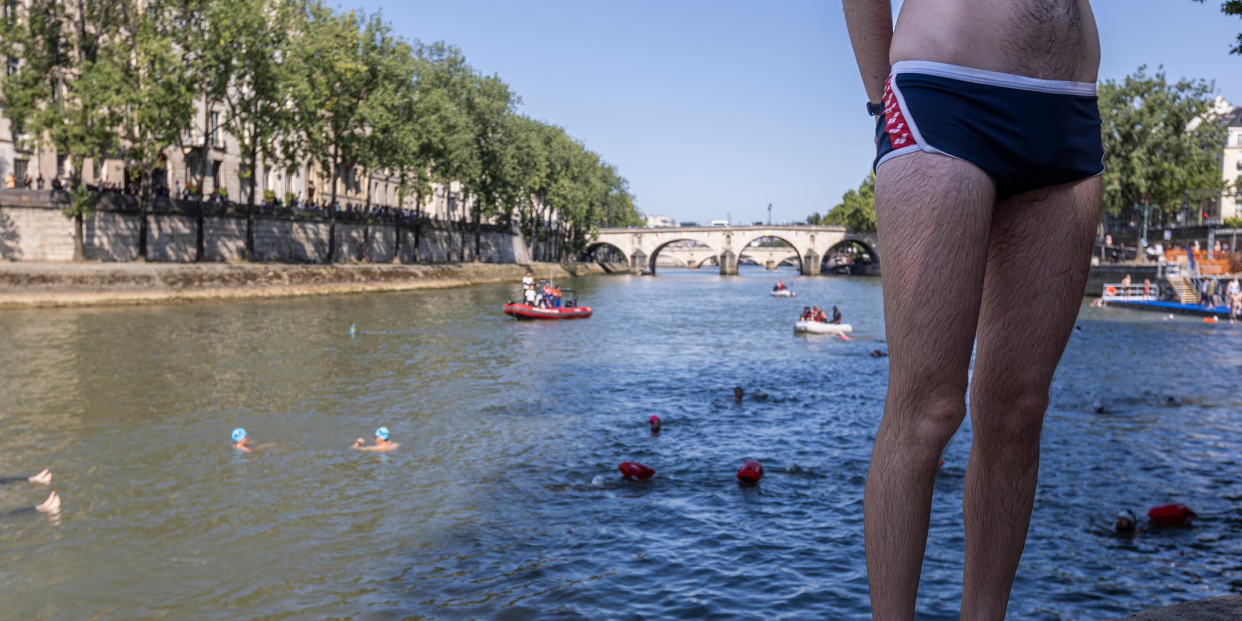A swimmer in trunks stands on the banks of the Seine.