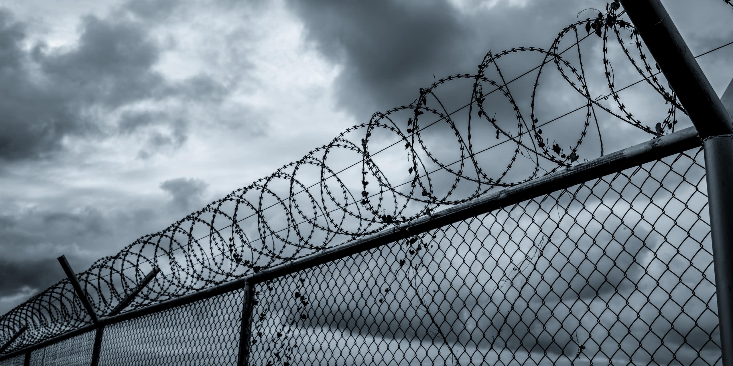 A prison security fence under a gloomy sky.