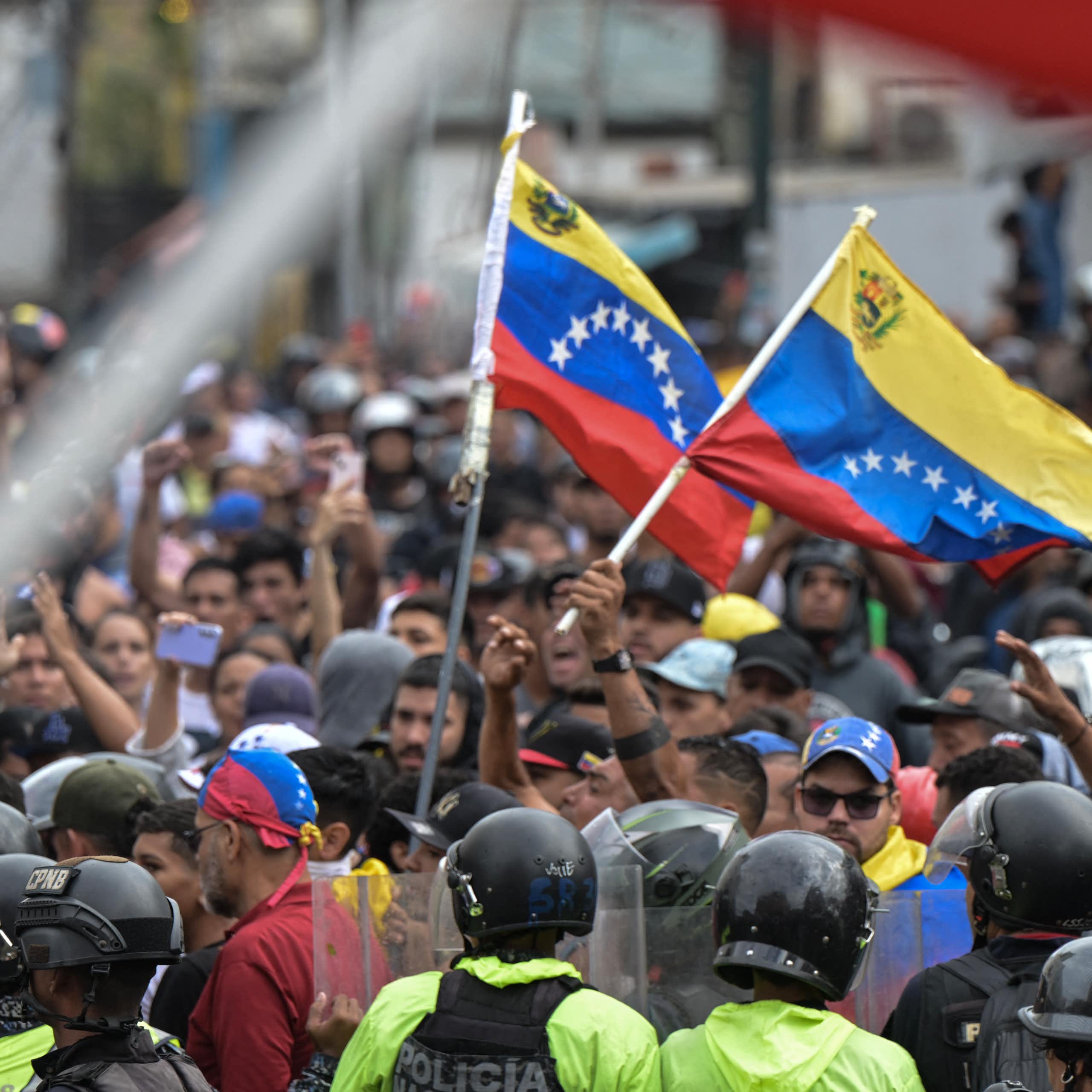 A group of protesters hold aloft flags while police look on.
