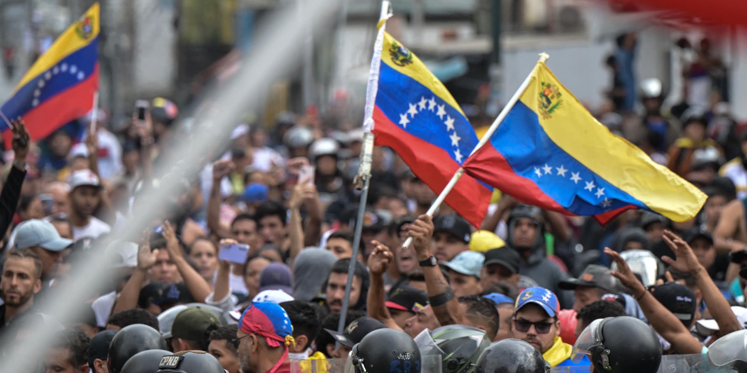 Um grupo de manifestantes segura bandeiras no alto enquanto a polícia observa.d aloft flags while police look on.