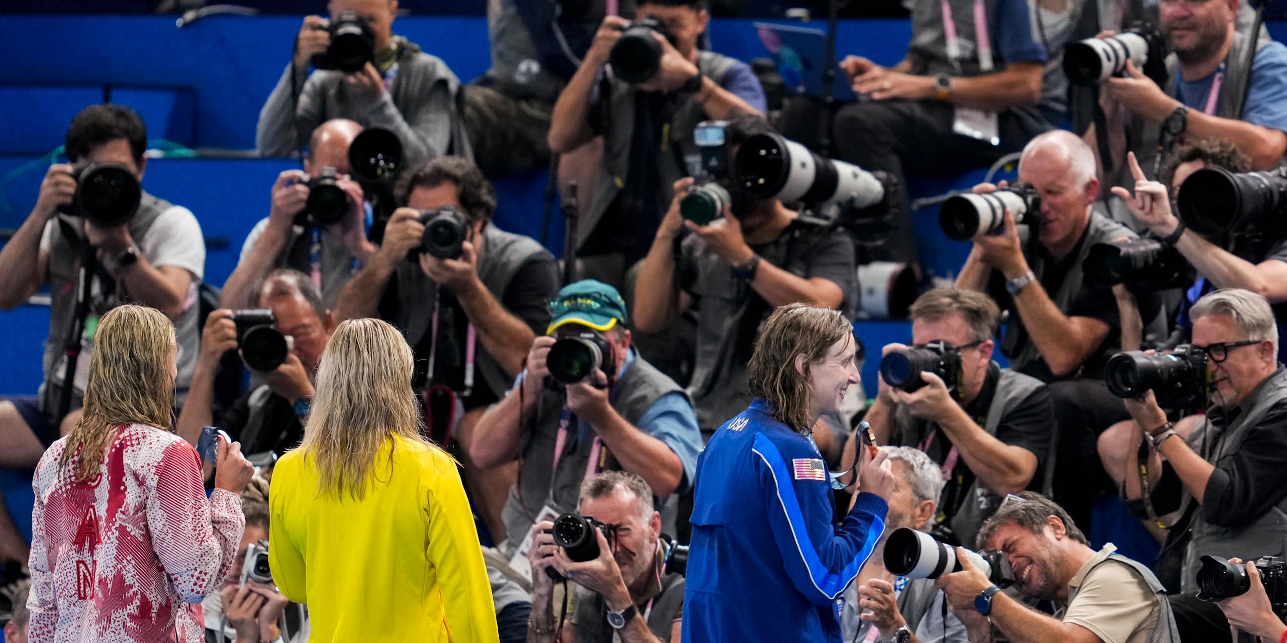 Three women stand in front of a wall of photographers