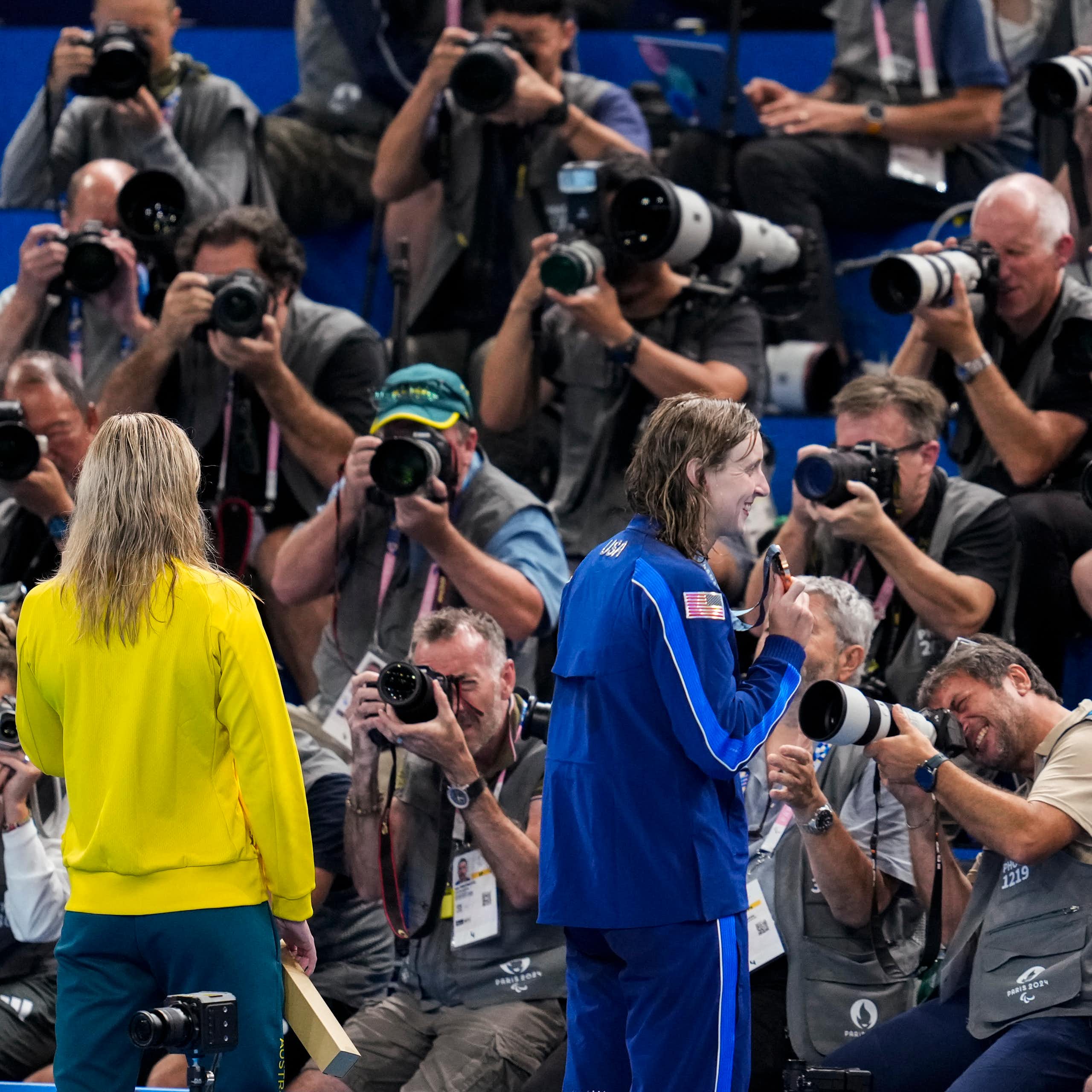 Three women stand in front of a wall of photographers