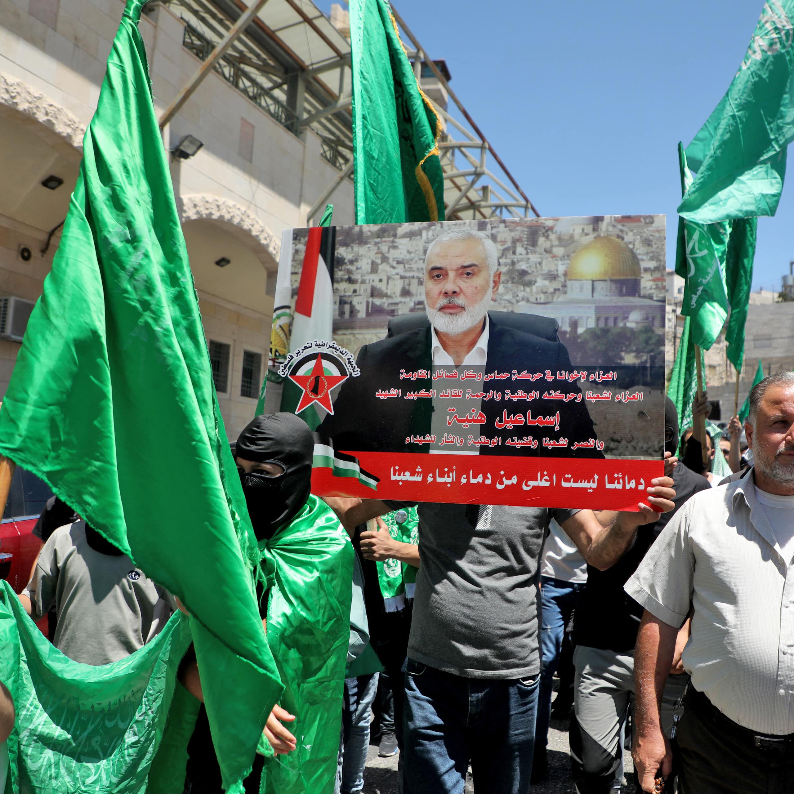 Men holding green flags hold aloft a photo of a man in a suit with a beard.
