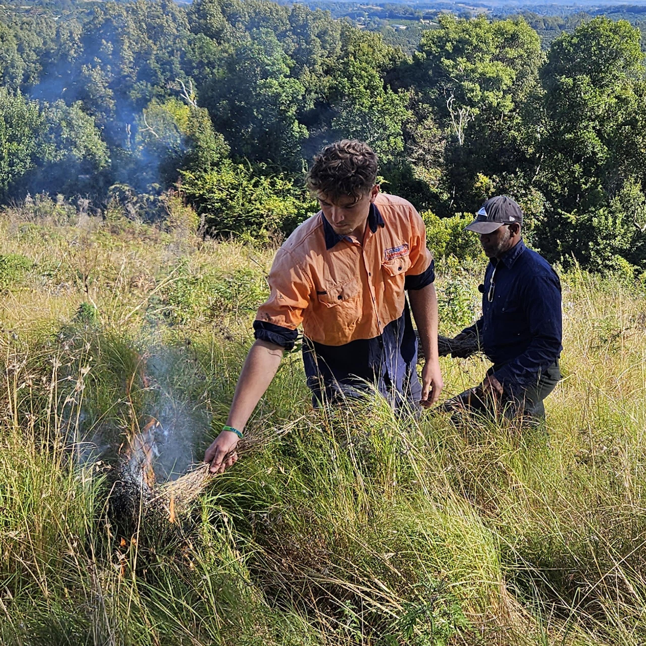 man lights grass fire as another man watches