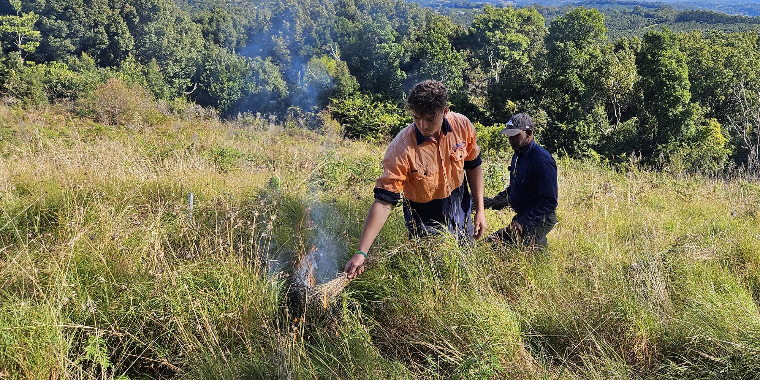 man lights grass fire as another man watches
